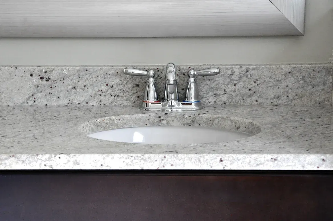 A bathroom sink with a granite counter top and a faucet.