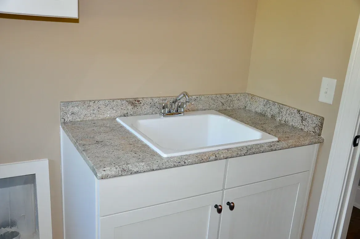 A bathroom sink with a granite counter top and white cabinets