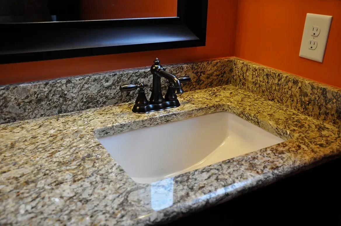 A bathroom sink with a granite counter top and a mirror.
