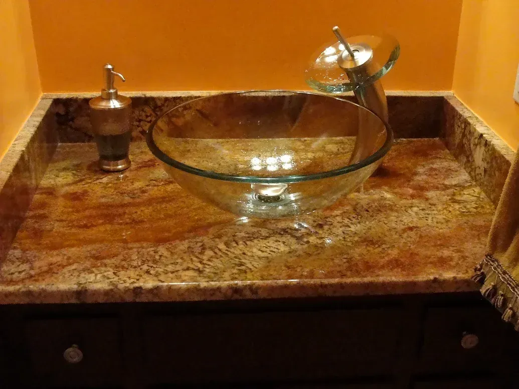 A bathroom sink with a glass bowl on a granite counter top.