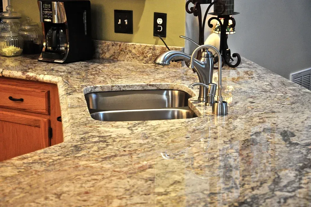 A kitchen sink with a stainless steel faucet on a granite counter top.