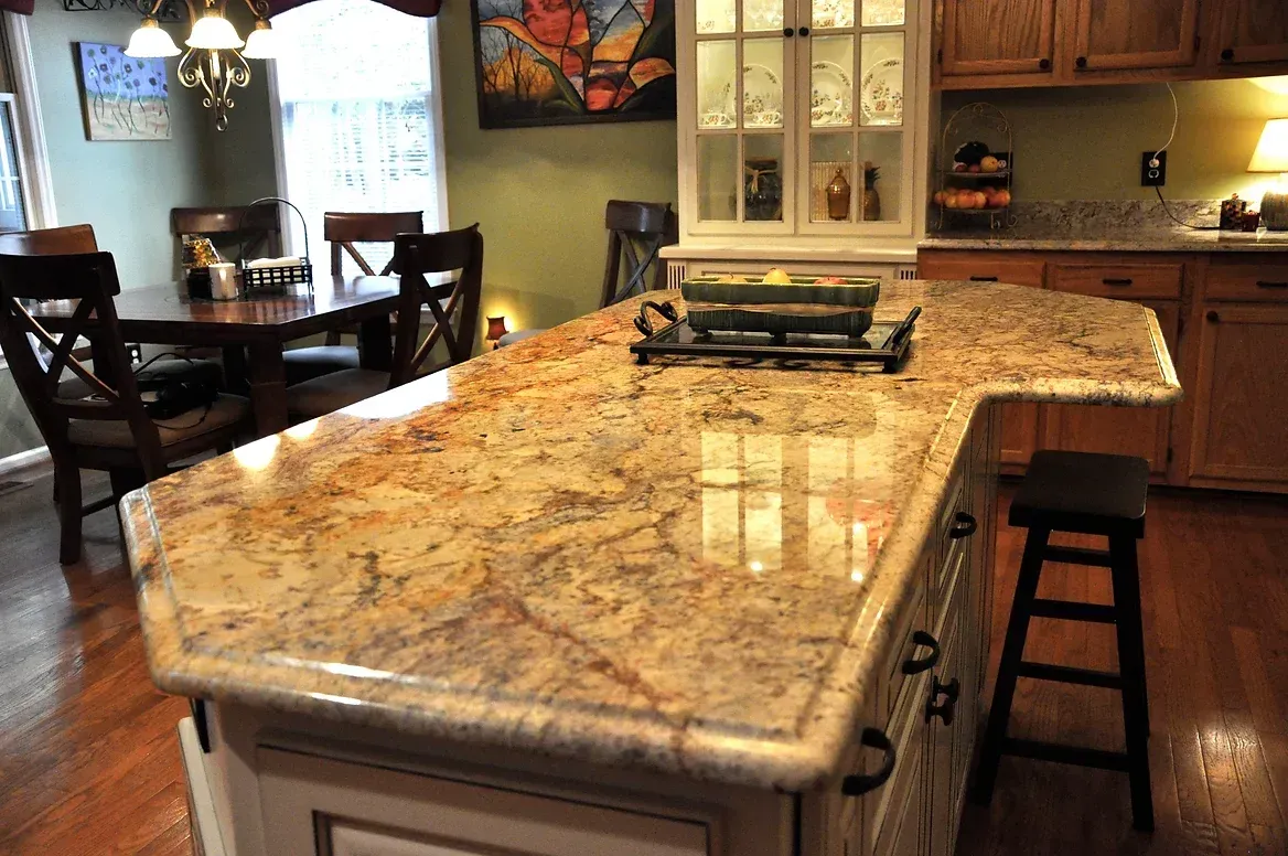 A kitchen with a large granite counter top and a dining room in the background.