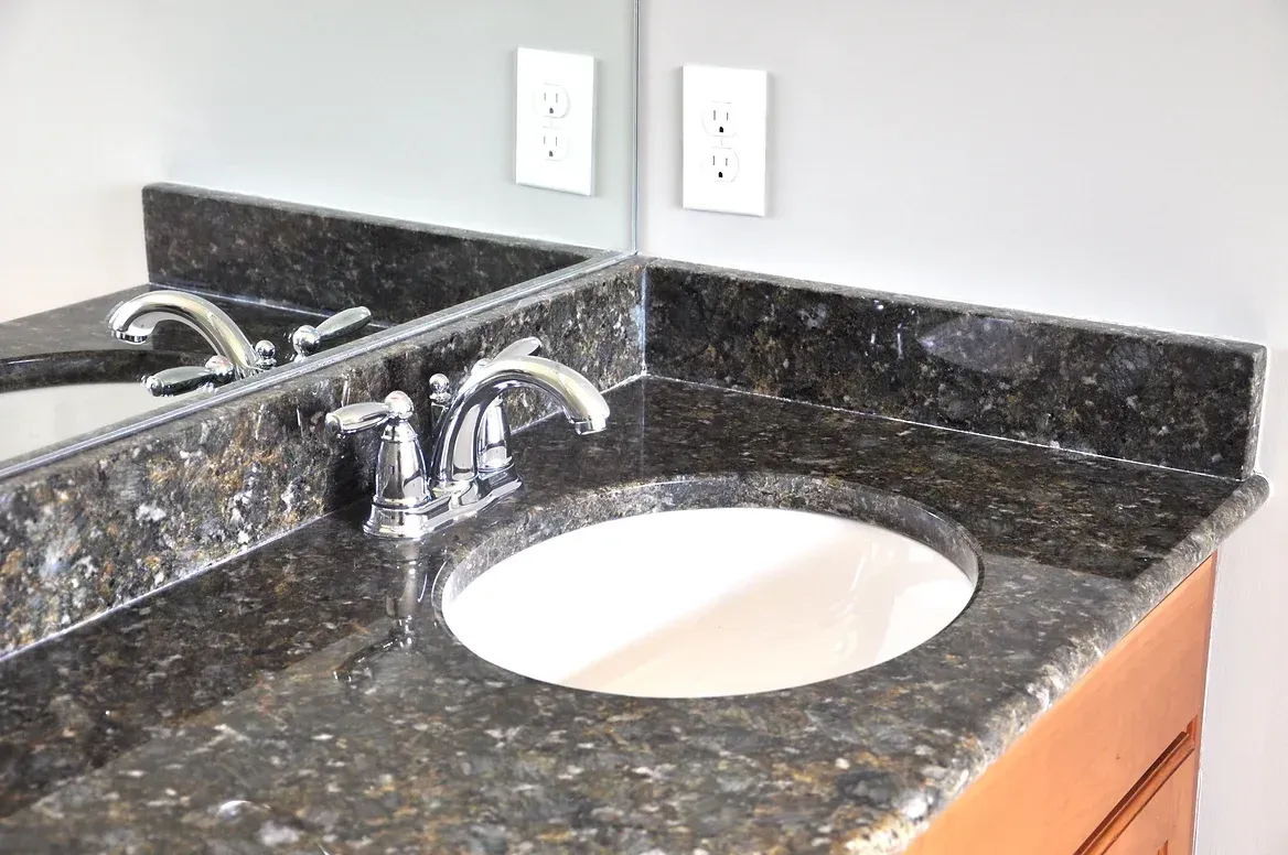 A bathroom sink with a black granite counter top and a mirror.