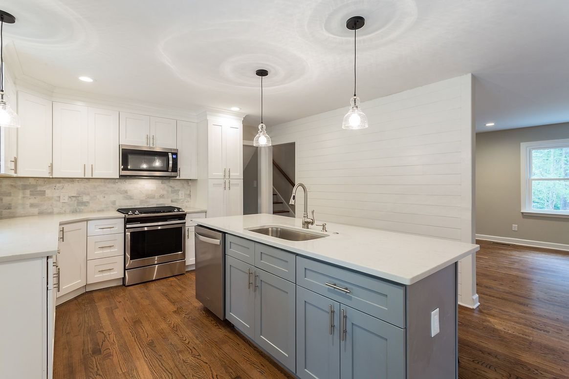 A kitchen with a large island , stainless steel appliances , white cabinets and hardwood floors.