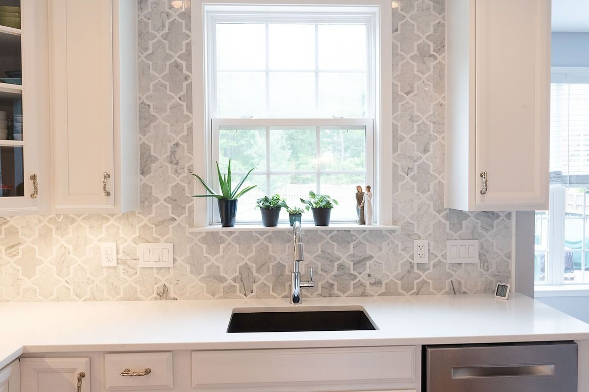 A kitchen with white cabinets , a sink , and a window.
