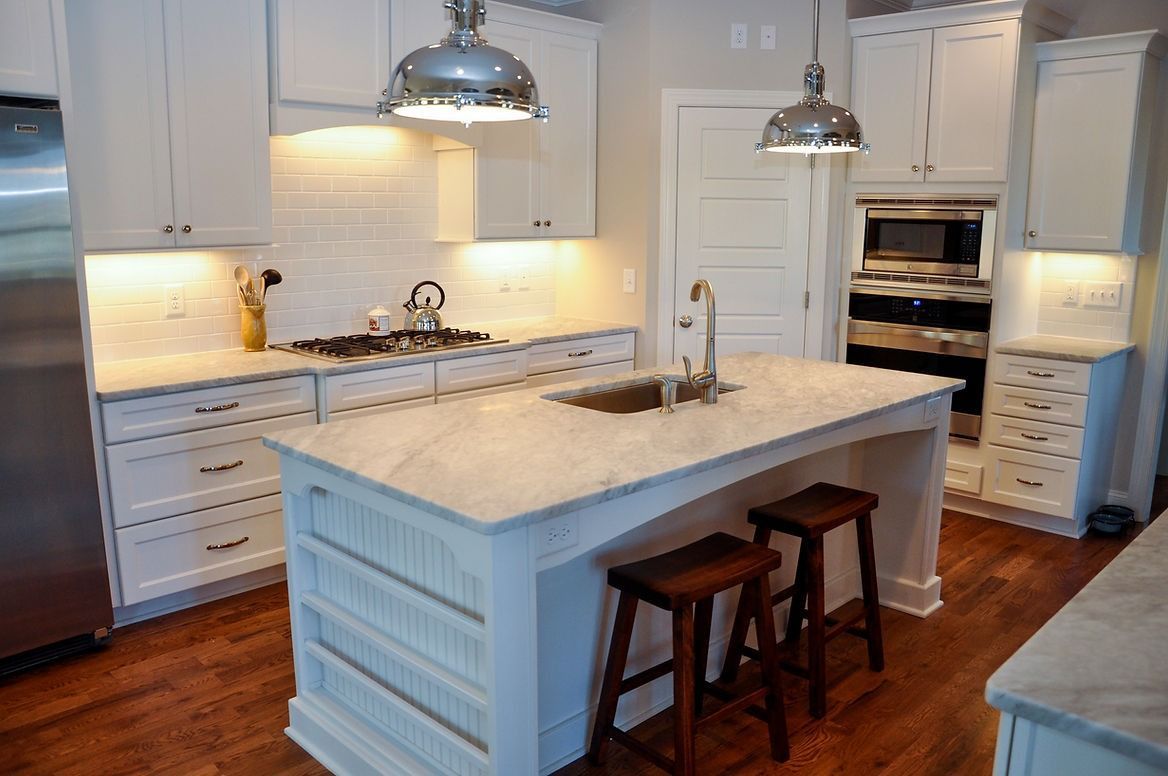 A kitchen with white cabinets , stainless steel appliances , and a large island.