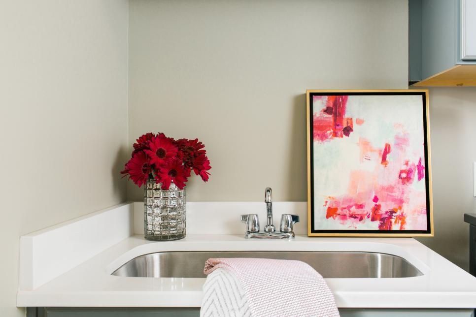 A kitchen sink with a vase of flowers and a painting on the wall.