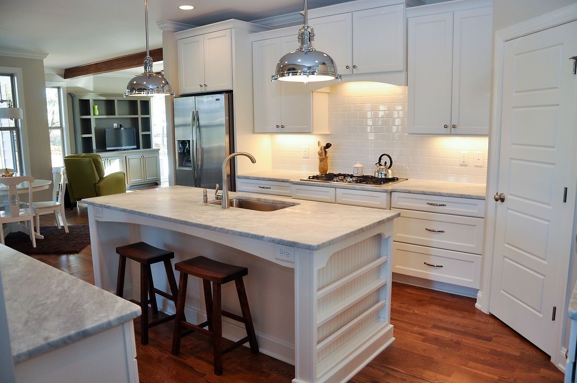 A kitchen with white cabinets , stools , a sink and a refrigerator.