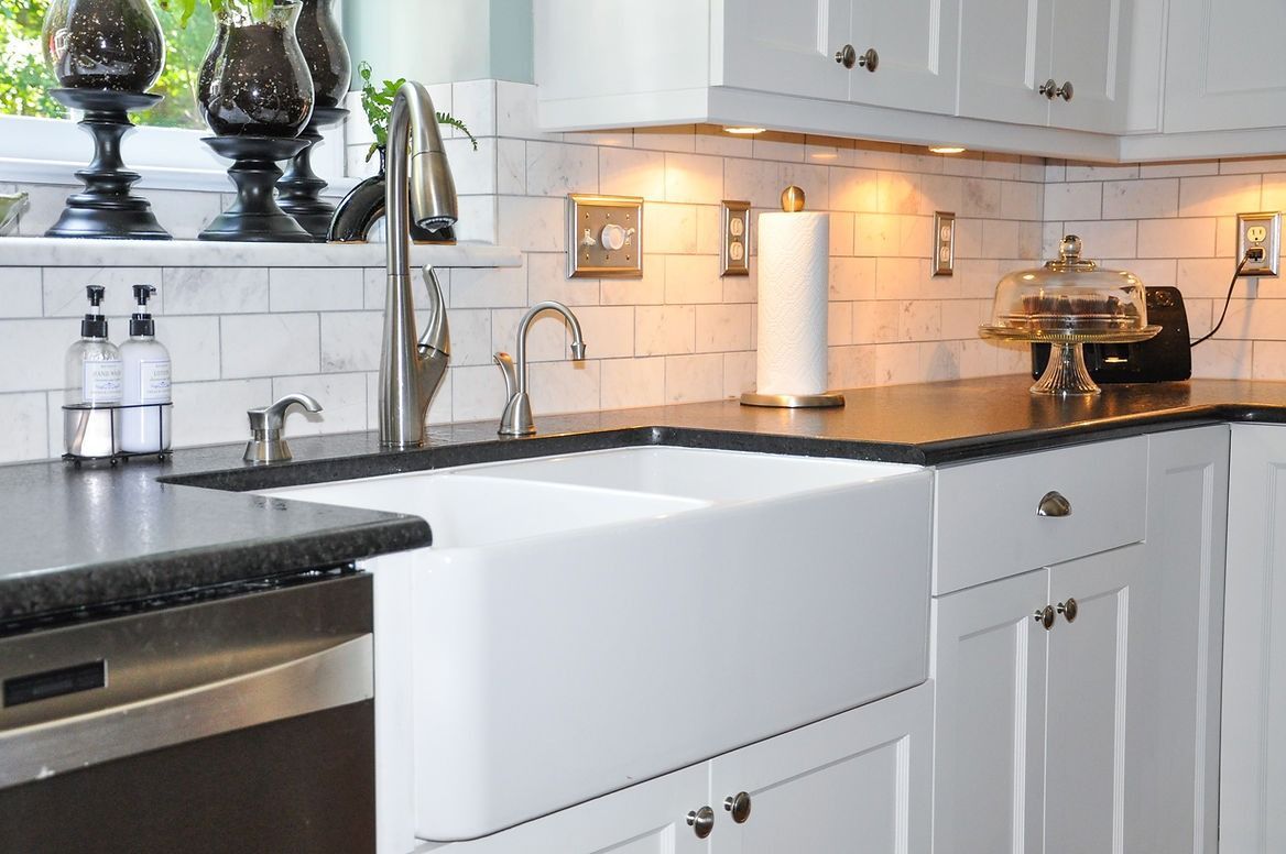 A kitchen with white cabinets , black counter tops , a sink and a dishwasher.