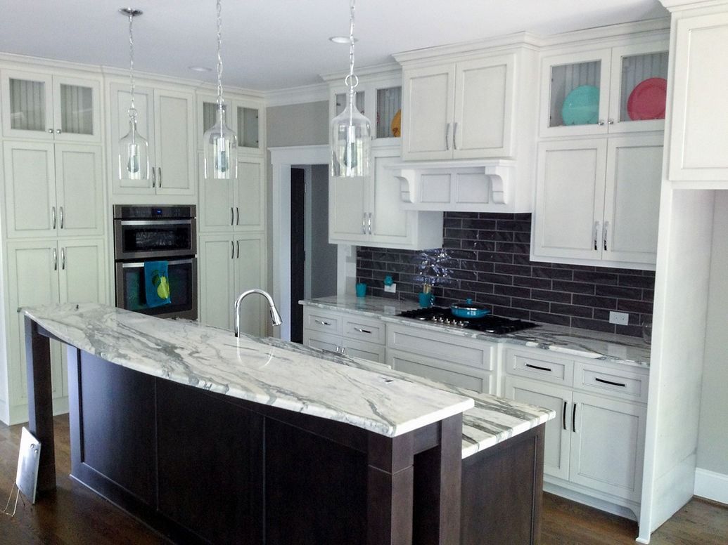 A kitchen with white cabinets , marble counter tops , and a large island.