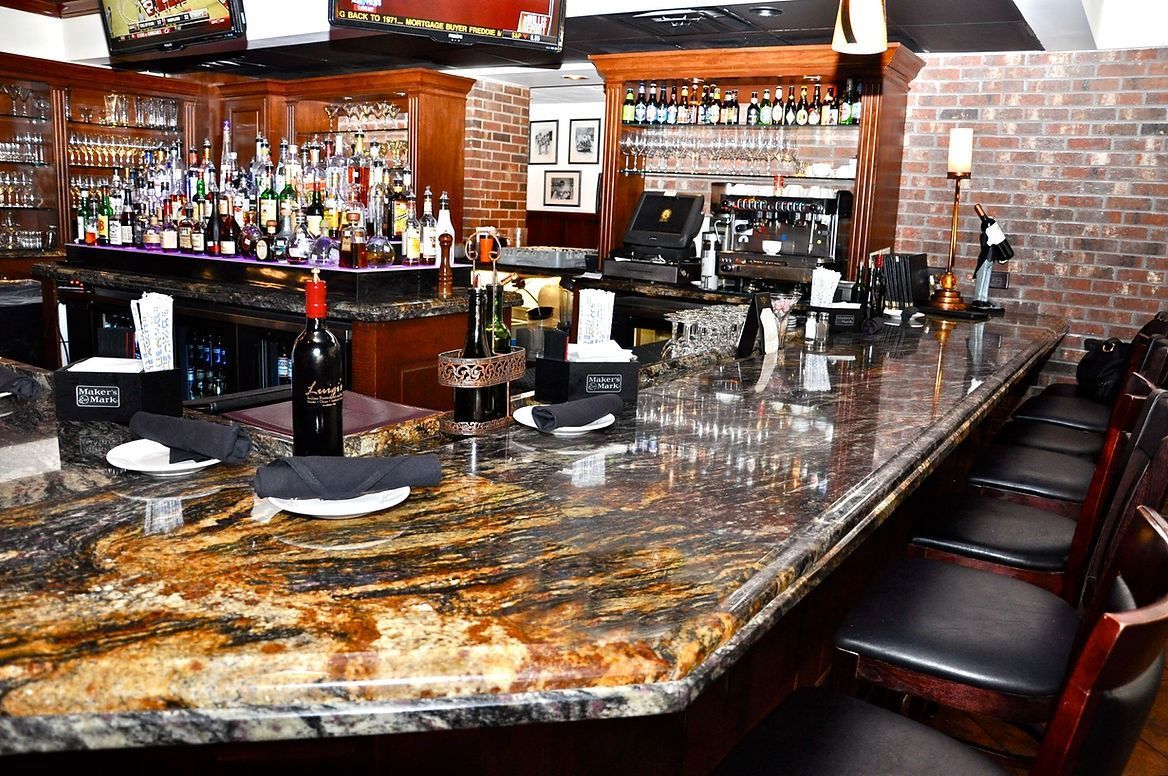 A long bar in a restaurant with a bottle of wine on the counter.