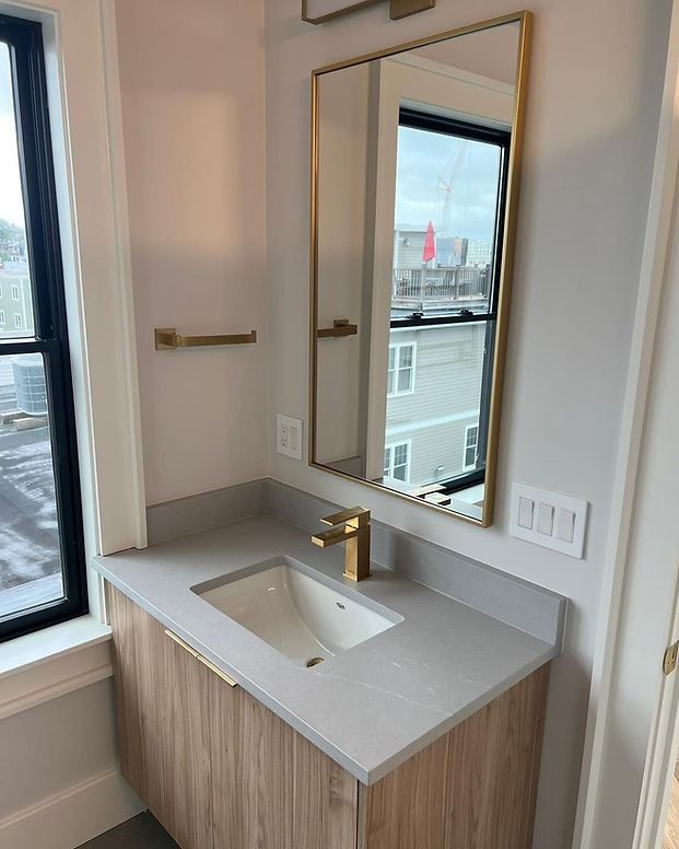 A bathroom with a sink , mirror and window.