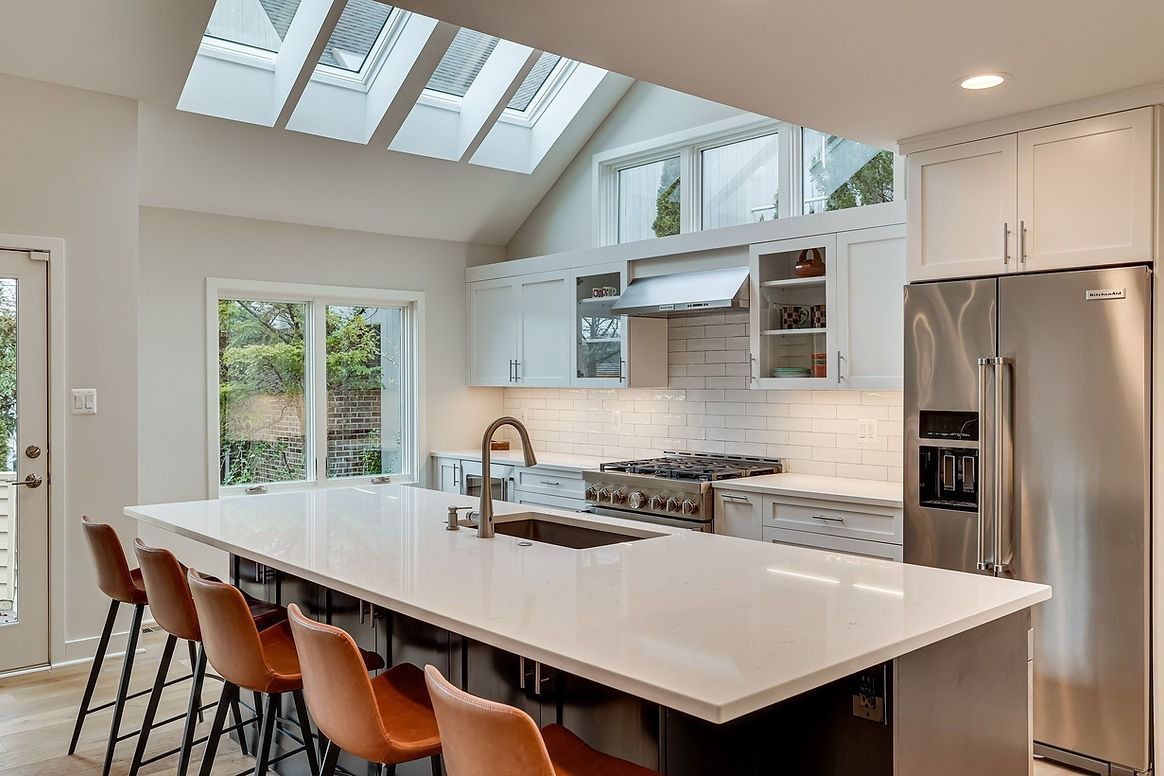 A kitchen with white cabinets , stainless steel appliances , a large island , and a skylight.