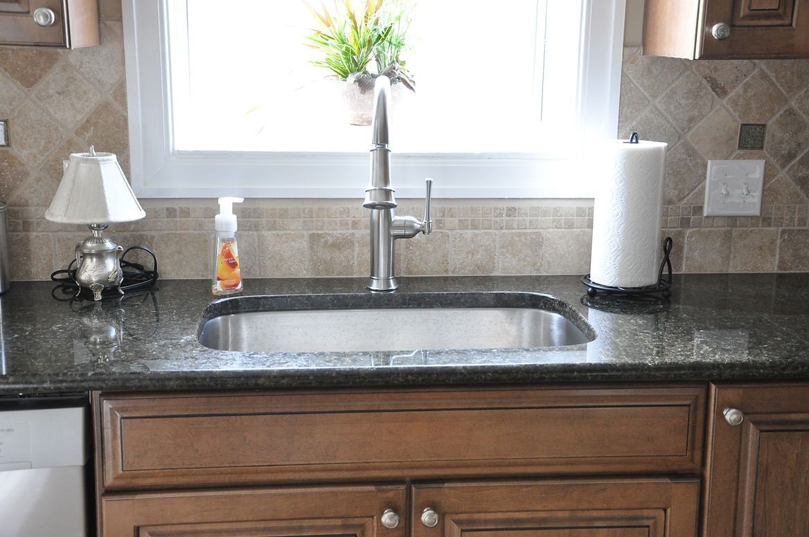 A kitchen sink with a soap dispenser and a paper towel holder on the counter.