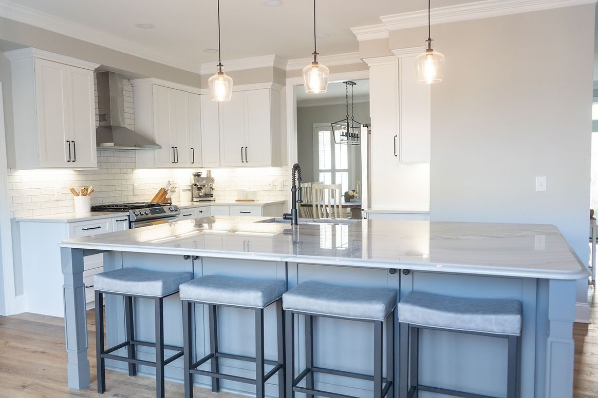 A kitchen with white cabinets and a large island with stools.