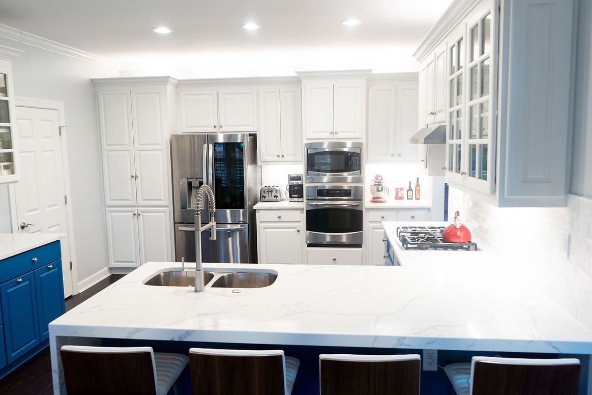 A kitchen with white cabinets , blue cabinets , stainless steel appliances and a large island.