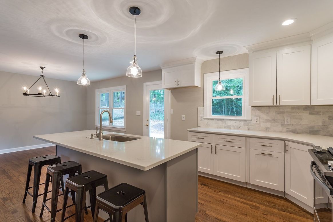 A kitchen with white cabinets , stools , a sink and a stove.