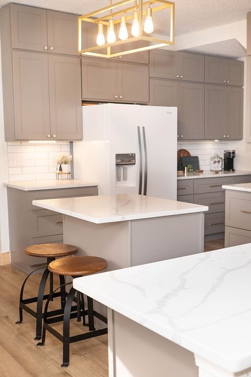 A kitchen with a large island , stools , a refrigerator and a chandelier.