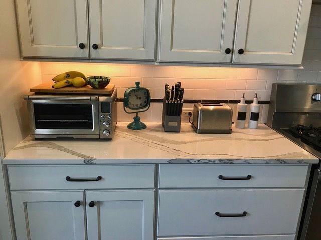 A kitchen with white cabinets , a microwave , a toaster oven , and a clock on the counter.