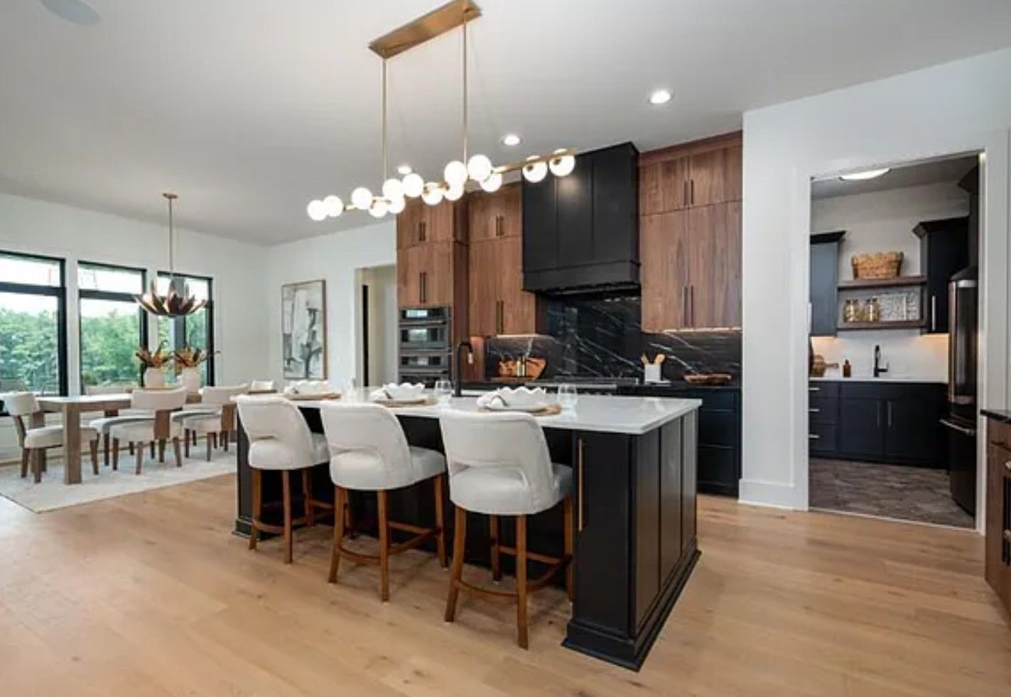 Modern kitchen with island, dining area, and dark wood cabinets; light wood floor.