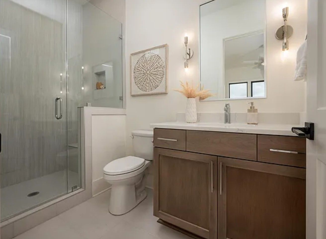 Bathroom with glass shower, wooden vanity, toilet, mirror, and decorative wall art.