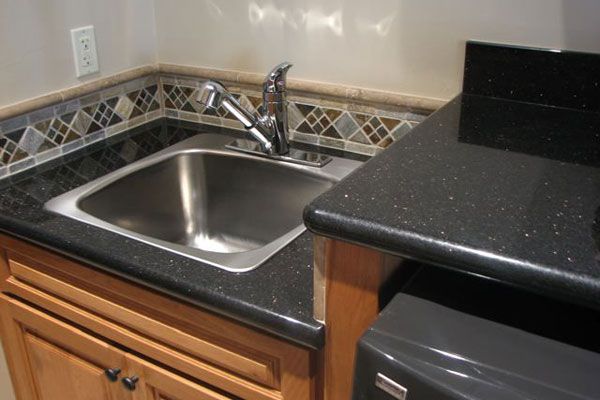 A kitchen with a stainless steel sink and a black counter top