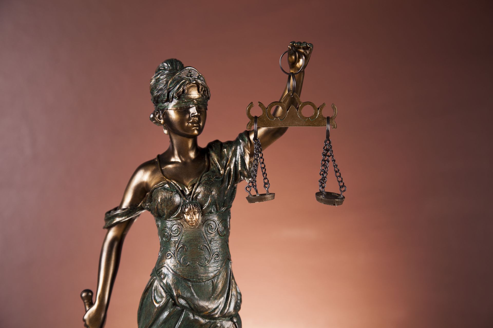 Bronze statue of Lady Justice holding scales, set against a brown backdrop.