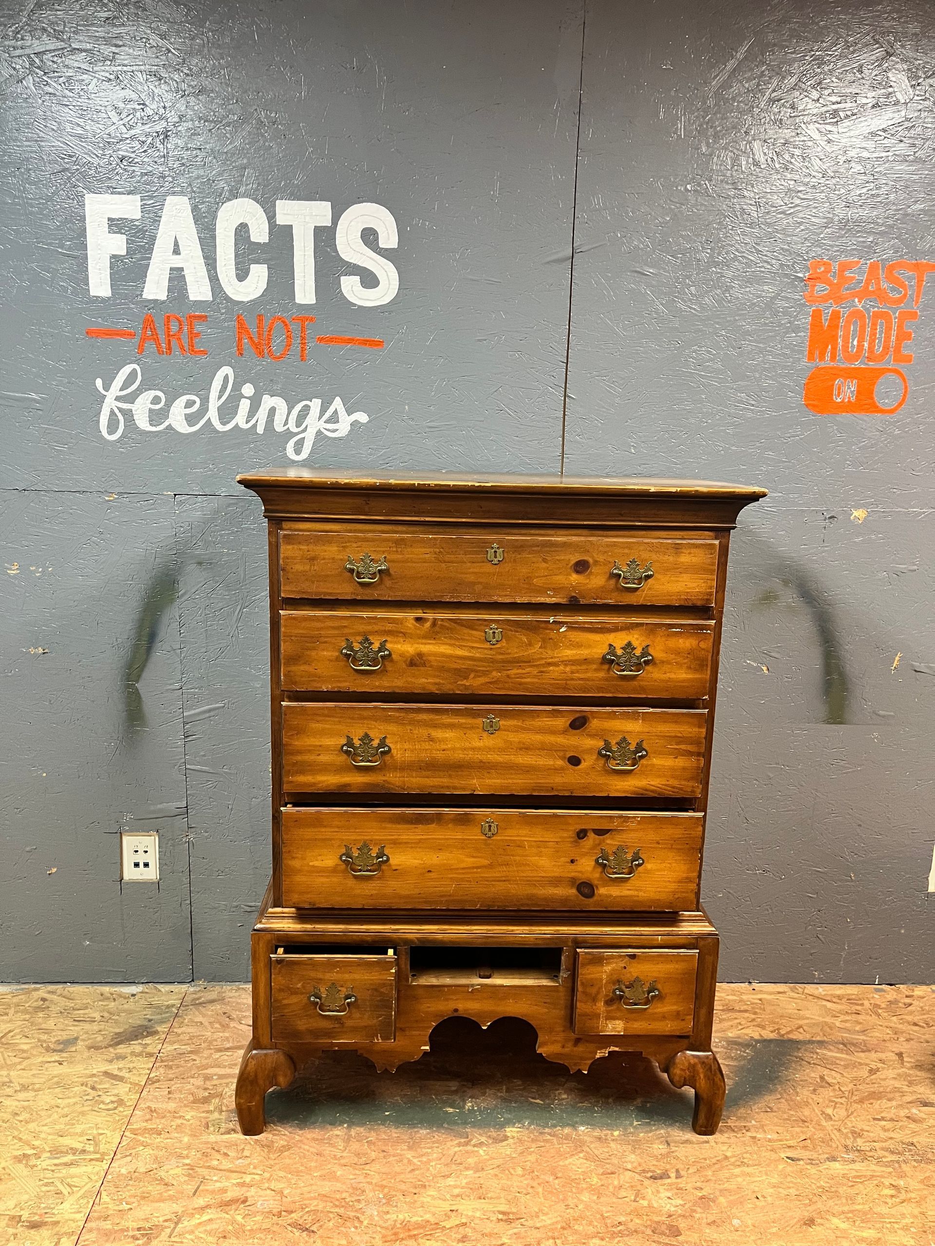 A wooden chest of drawers is sitting in front of a wall that says facts are not feelings.