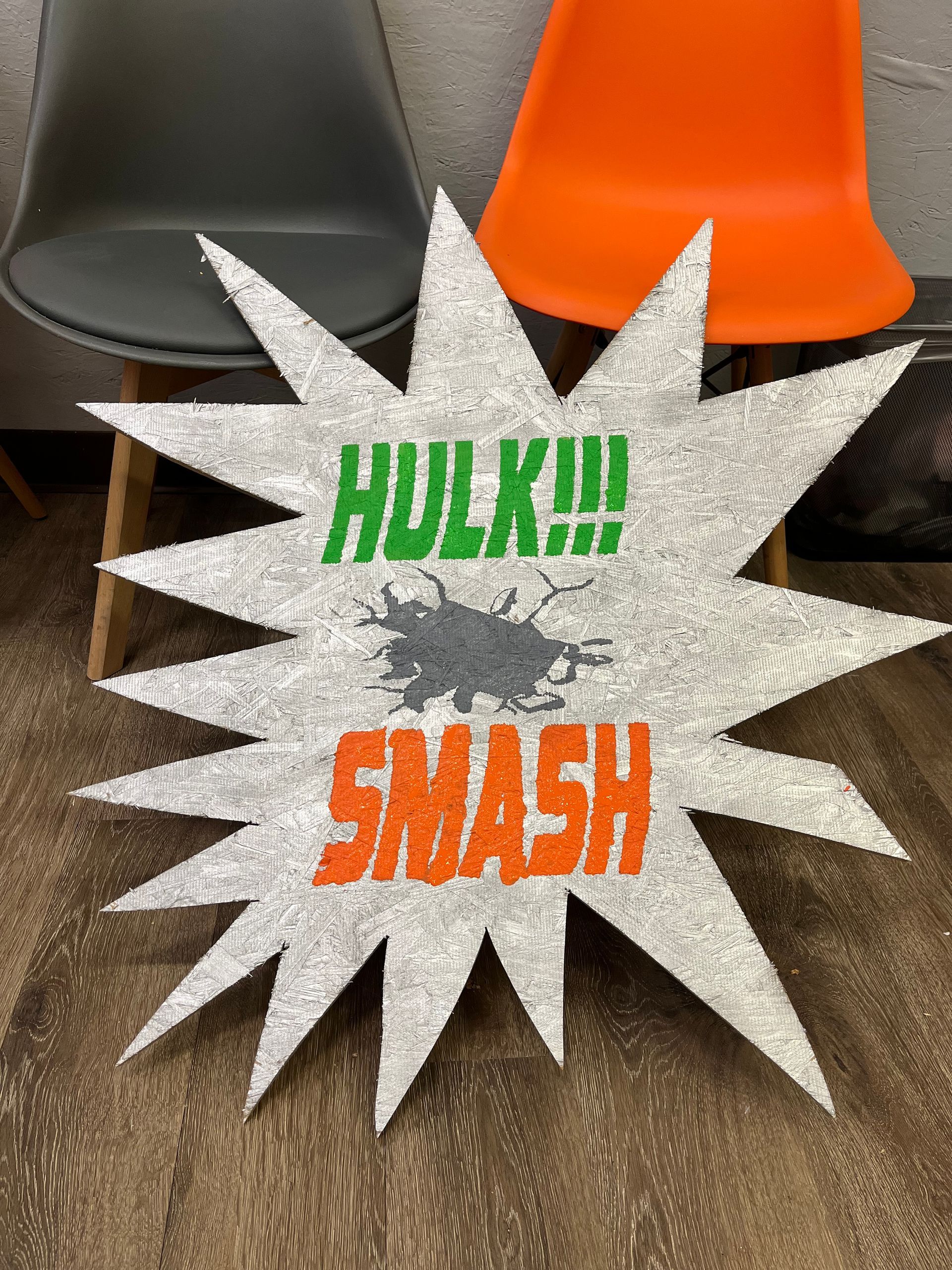 A sign that says hulk smash is sitting on the floor next to two chairs.