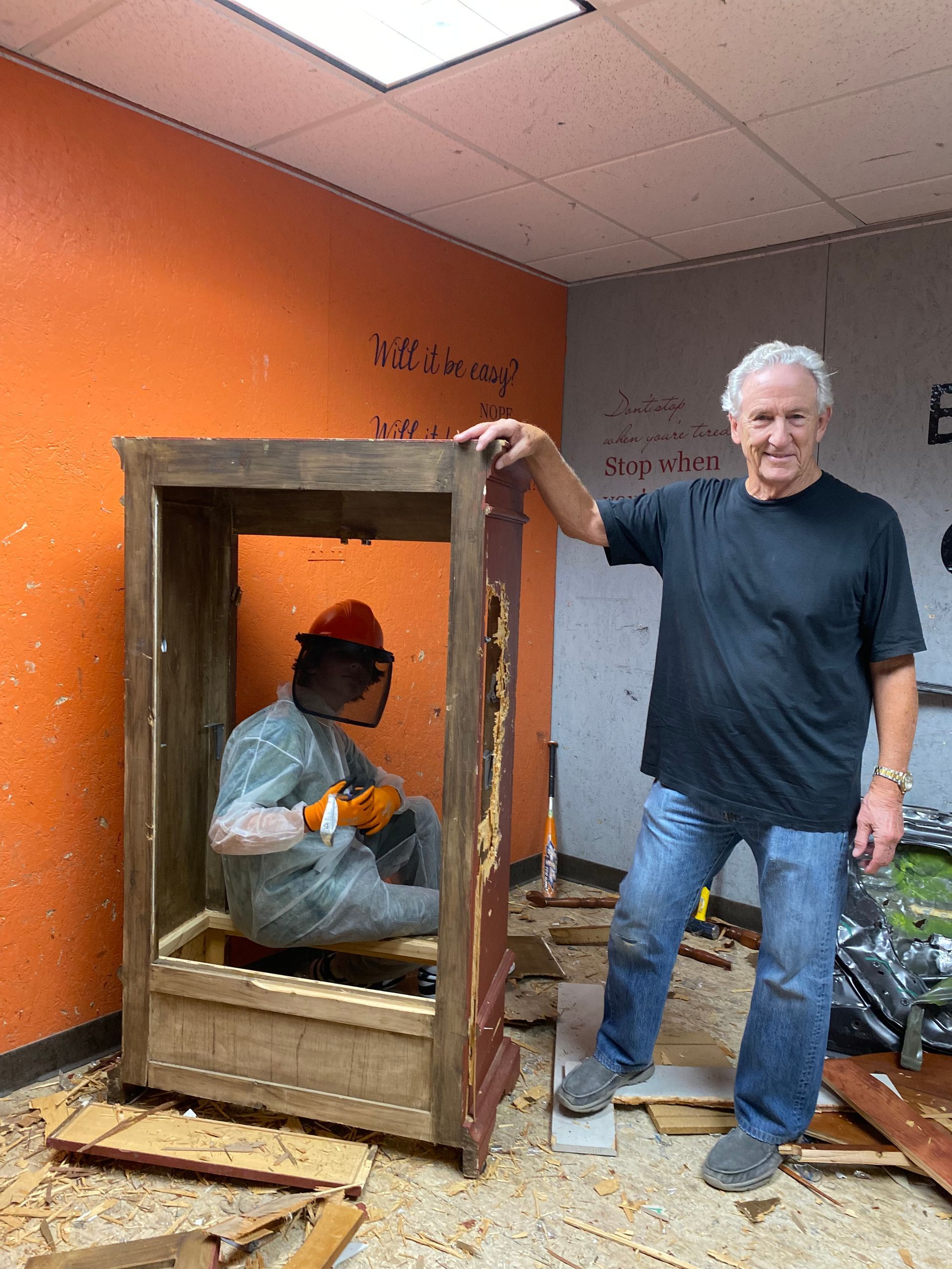 A man is standing next to a man sitting in a wooden box.