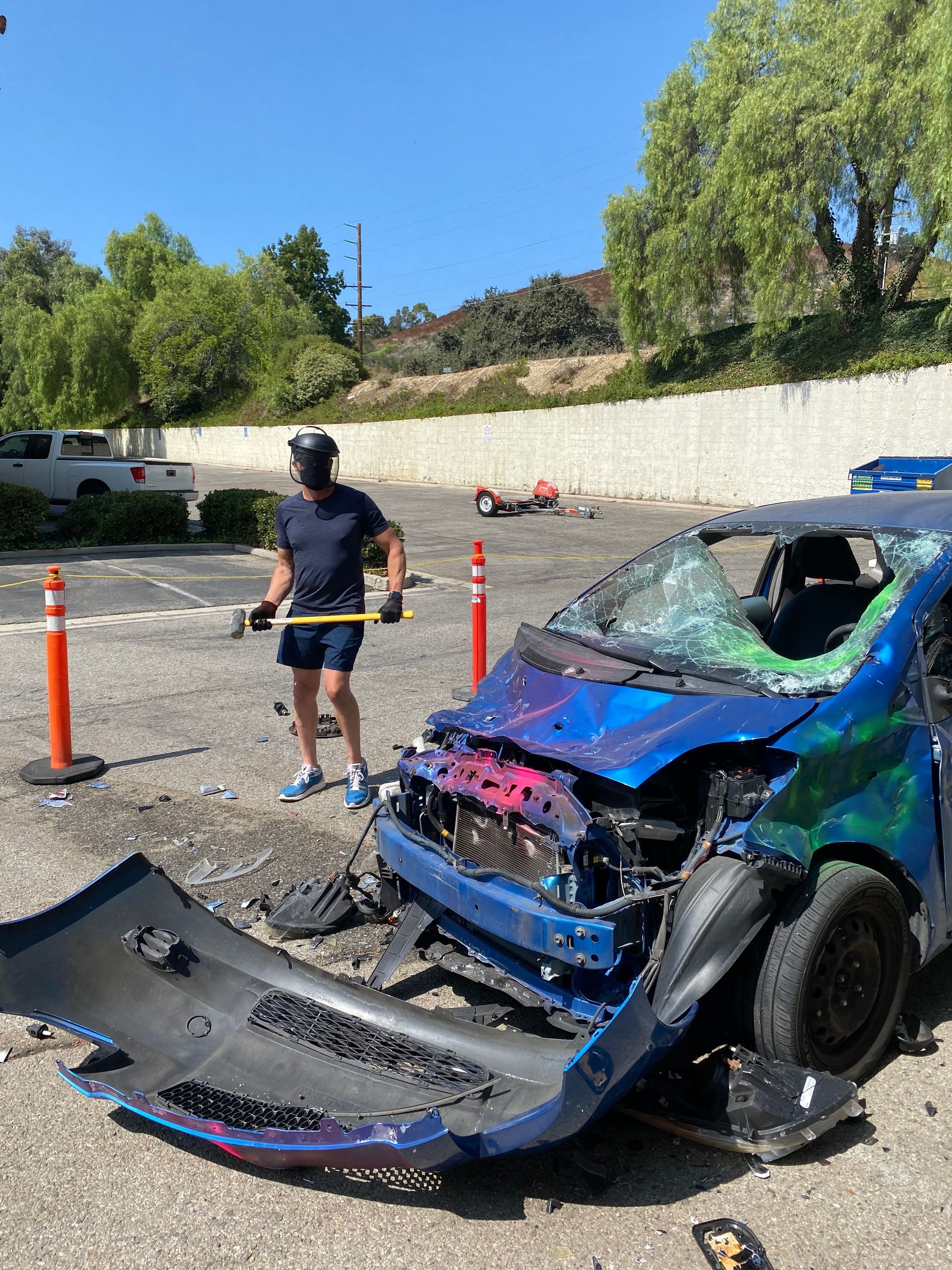 A man is standing next to a damaged car in a parking lot.