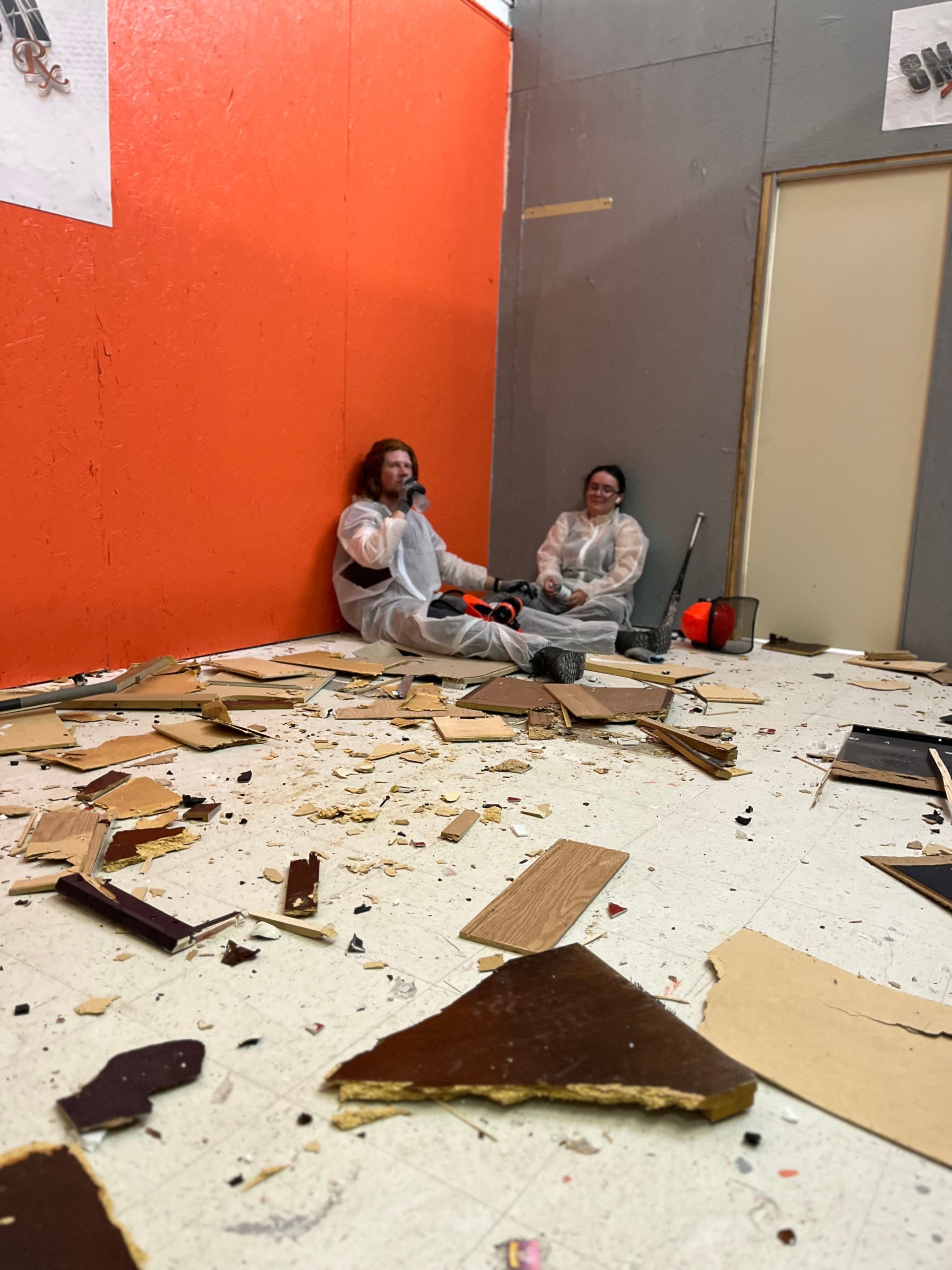 Two people are sitting on the floor in a messy room