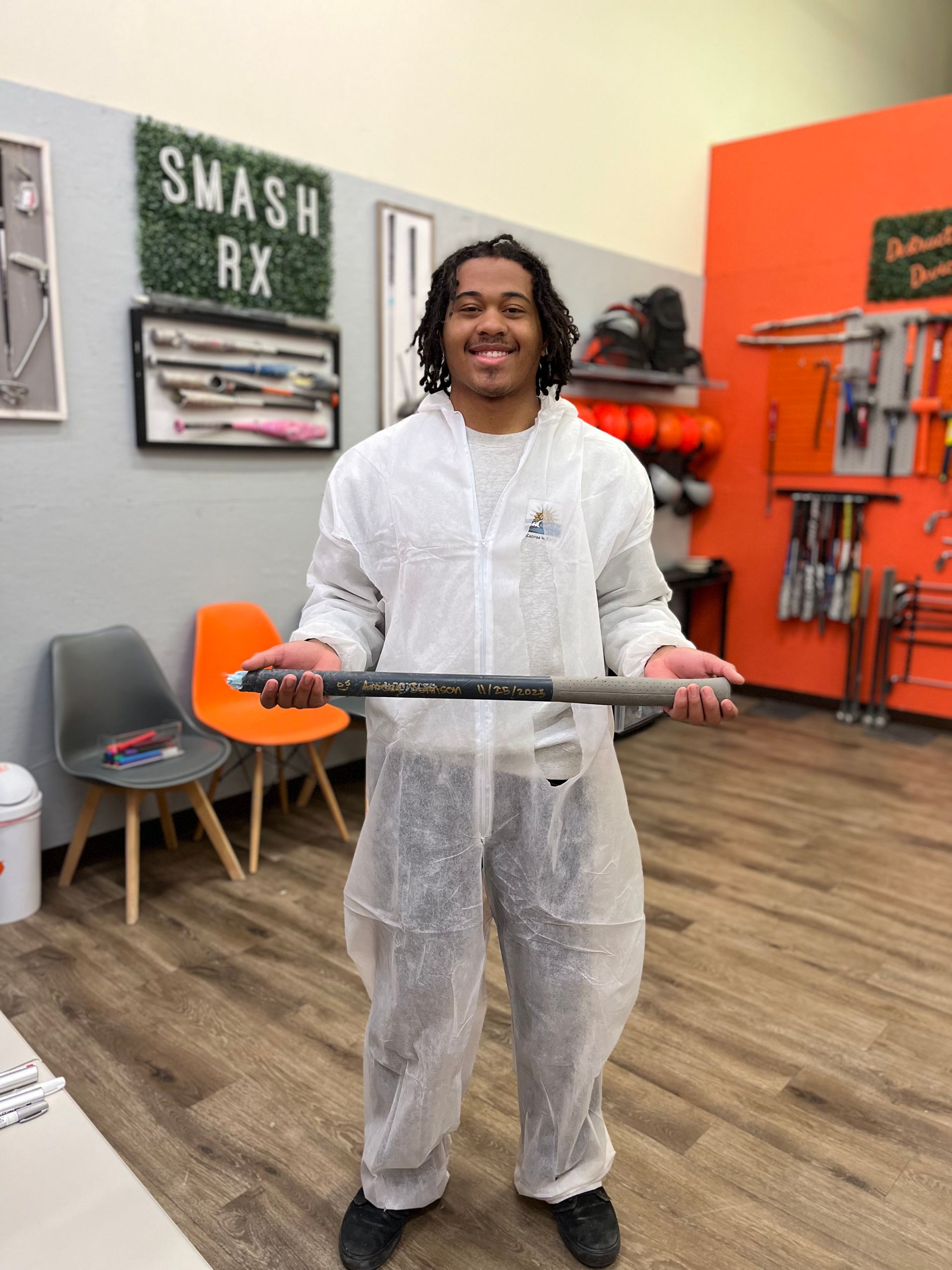A man in a white coveralls is holding a bat in a room.