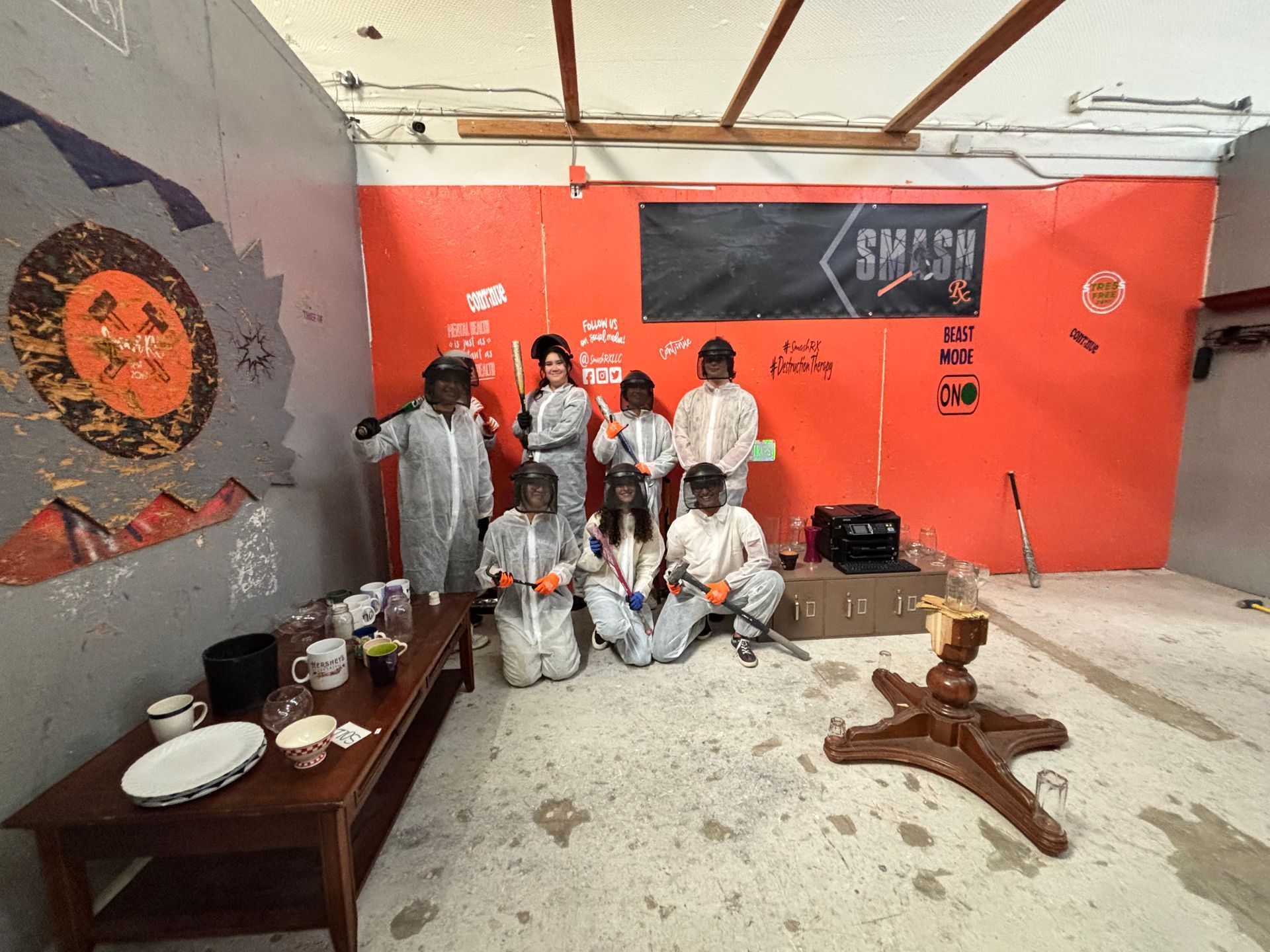 Group in protective suits, posing in a smash room