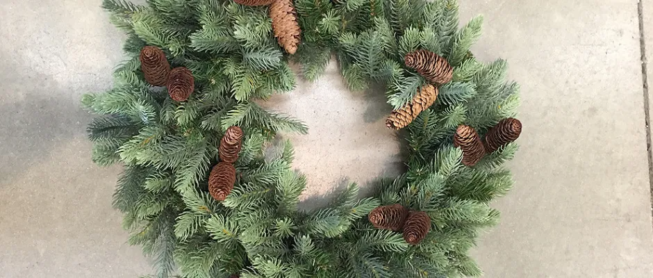 A Christmas wreath made of green fir with pinecones on a light-colored surface.