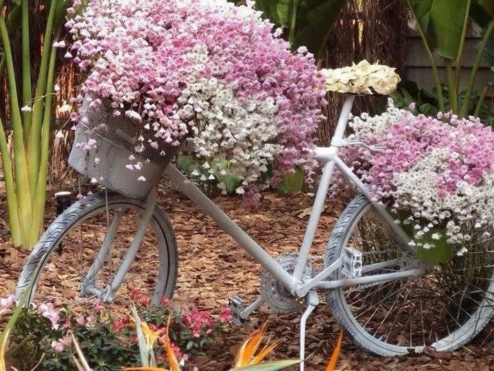 White bicycle overflowing with pink and white flowers in a garden setting.