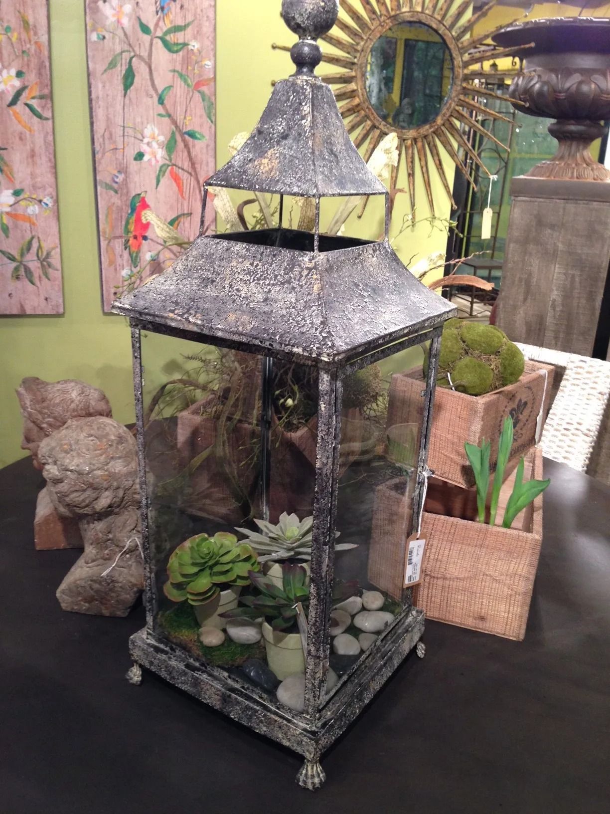 Terrarium in a weathered metal lantern, with greenery and decorative stones.