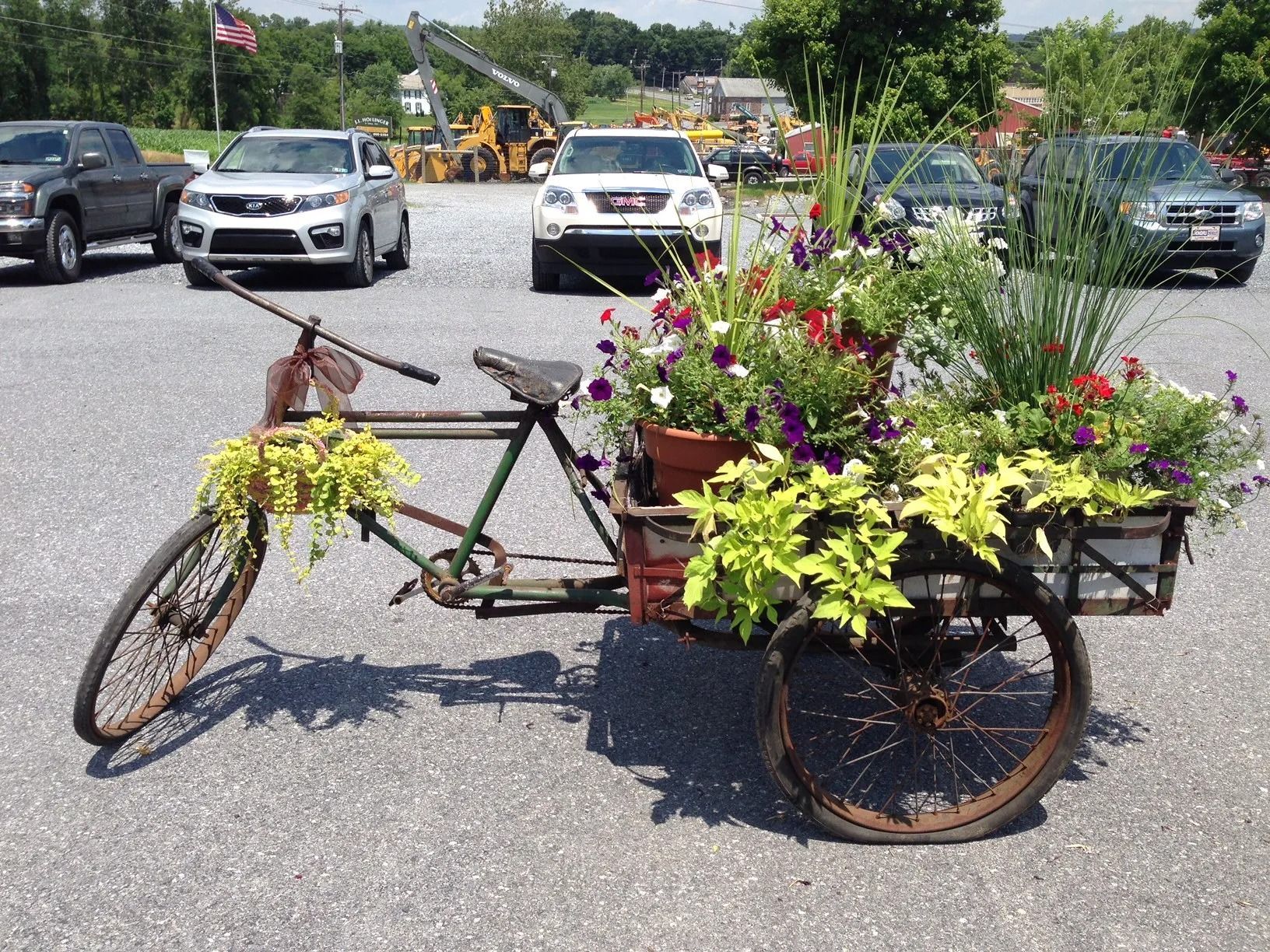 Antique bicycle with flower baskets in a parking lot with cars and construction equipment.