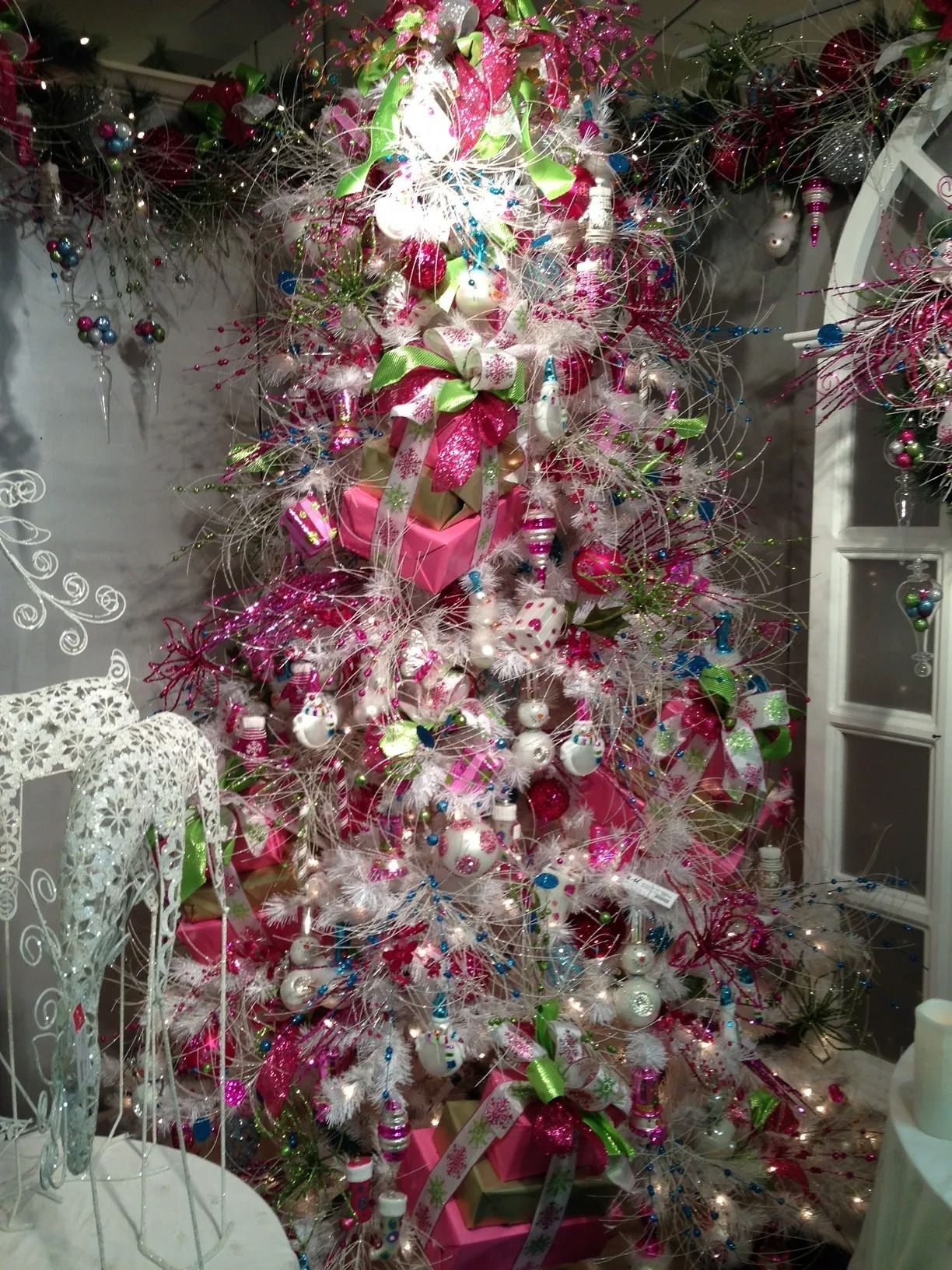 Christmas tree with pink, white, and blue ornaments and wrapped gifts, in a decorated display.