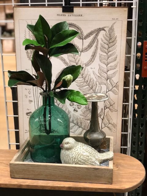 Green vase with foliage, small bird, and vintage botanical print on wooden tray.