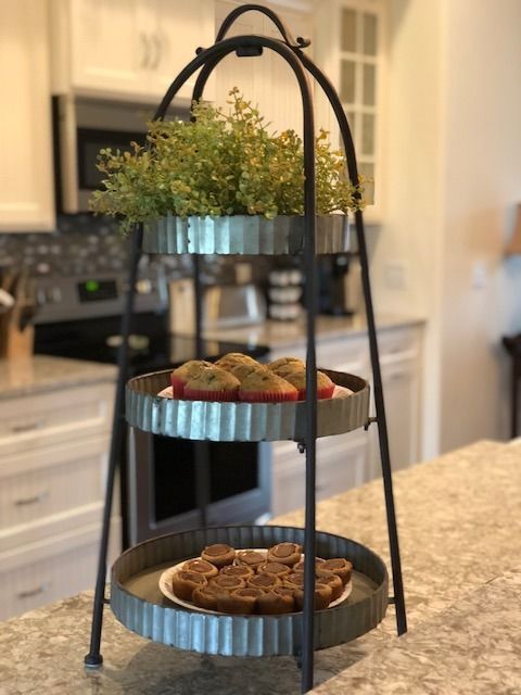 Three-tiered metal serving tray with cookies and greenery on a kitchen countertop.