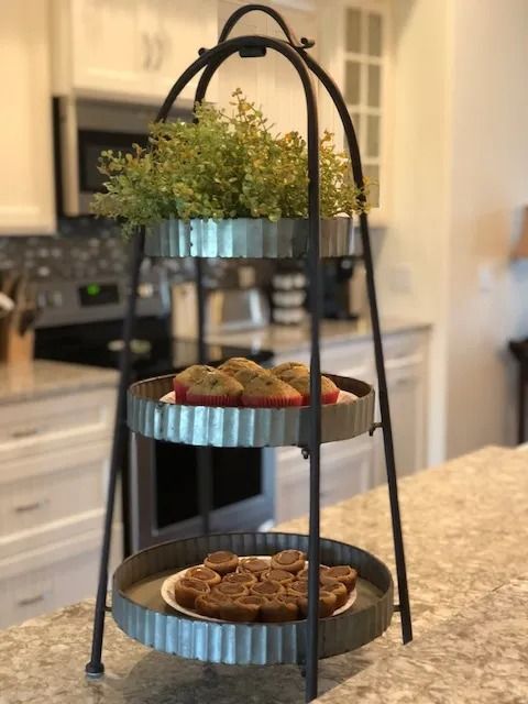 Three-tiered metal tray stand with treats and greenery in a kitchen.