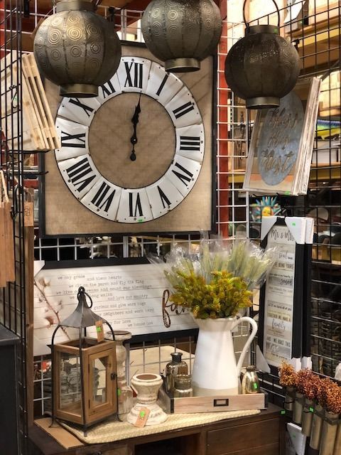 A display featuring a large clock, lanterns, a white pitcher with yellow flowers, and decorative items.