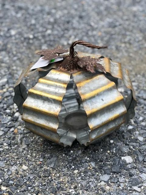 Metal pumpkin decoration with gold trim and leaves on gravel.