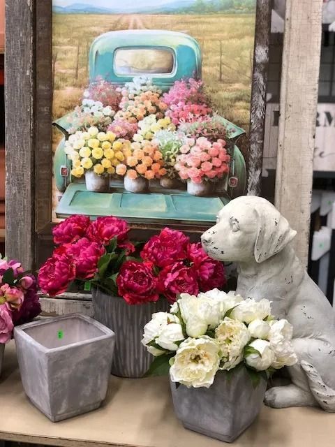 Flowers in vases with a painted truck and a dog statue, displaying springtime blooms.