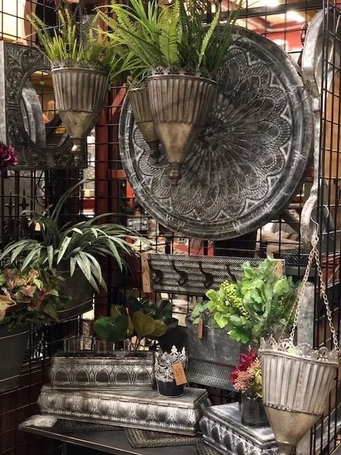 Display of rustic metal planters and decorative items on a grid, with greenery and flowers.