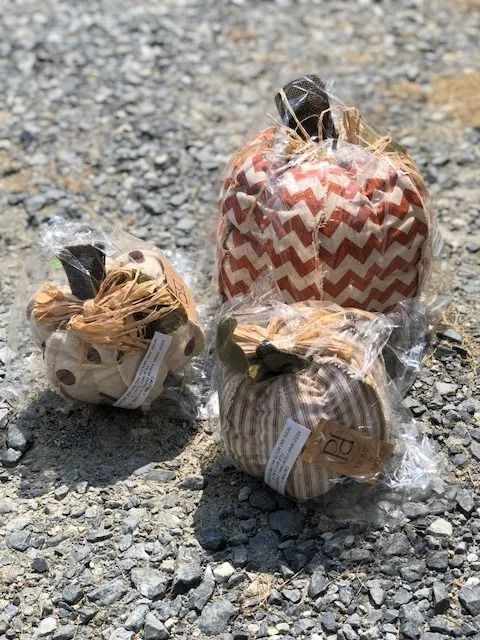 Three decorative fabric pumpkins in plastic wrap on gravel.