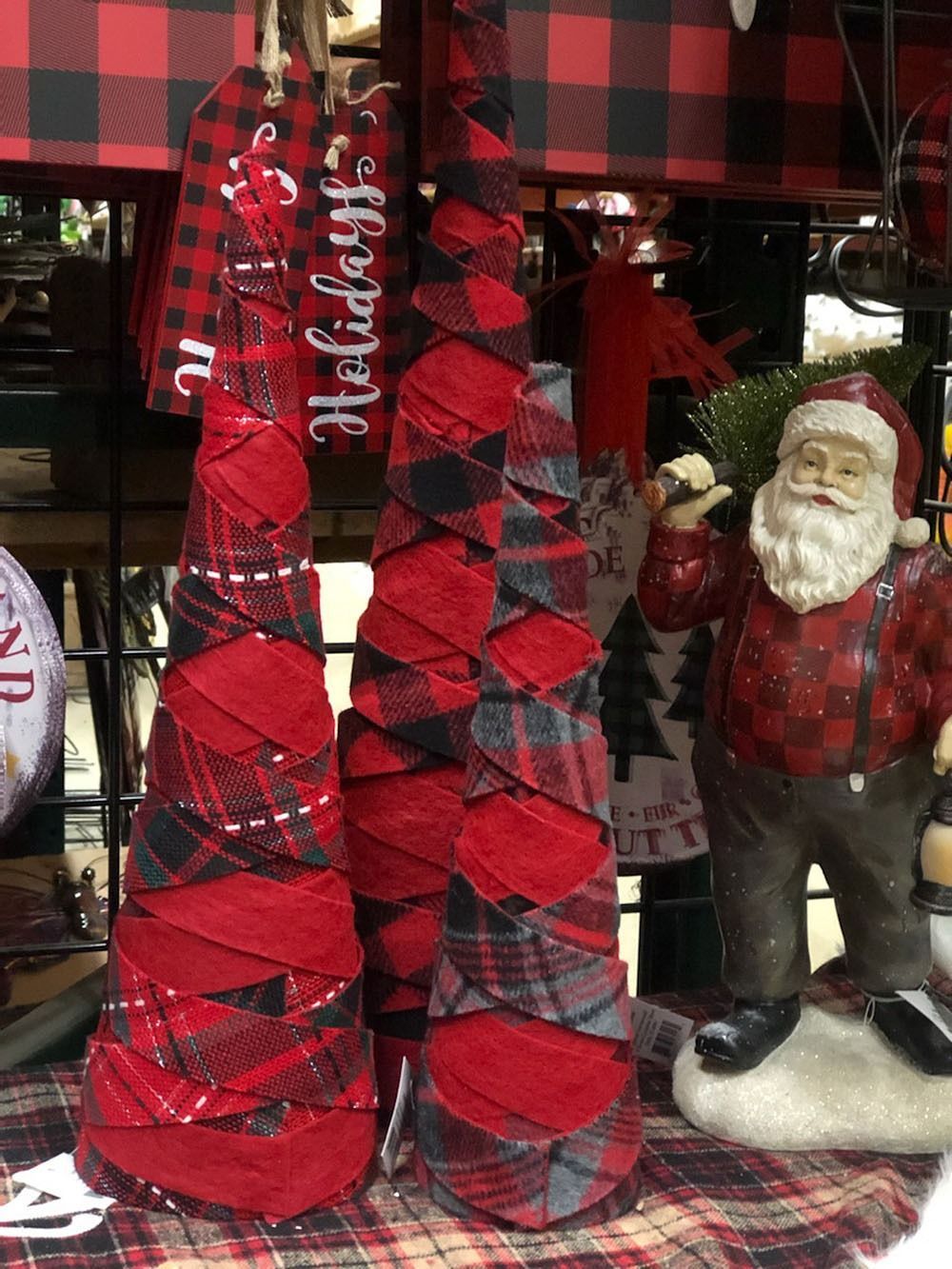 Three plaid fabric Christmas trees stand near a Santa figurine.