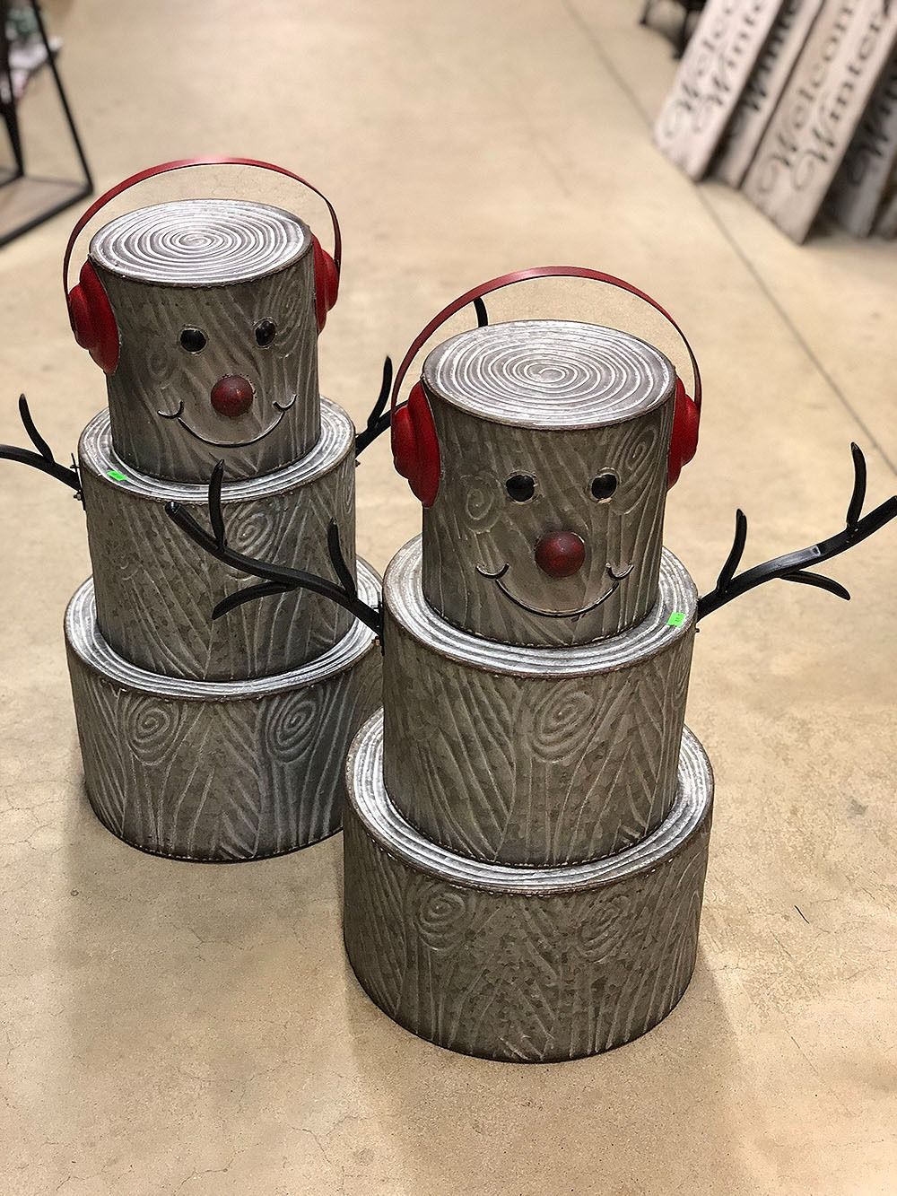 Two metal snowman decorations with red earmuffs, black twig arms, and smiling faces.