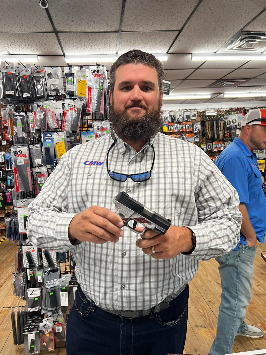 A guy wearing plaid shirt holding a gun inside the gun store.